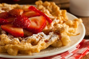 Homemade funnel cakes with powdered sugar and strawberries on top.