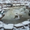 A frozen rock garden pond with a ceramic frog.