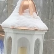 A white birdfeeder with a copper roof and a pillar candle inside where the birdfood would normally go.