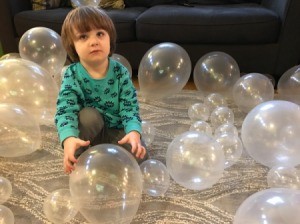 A 3 year old playing with clear balloons.