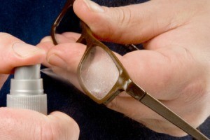 Spraying eyeglass cleaner on eyeglass lenses.