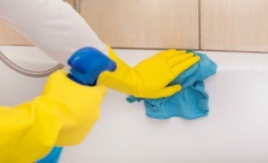 Person wearing rubber gloves cleaning a bathtub.