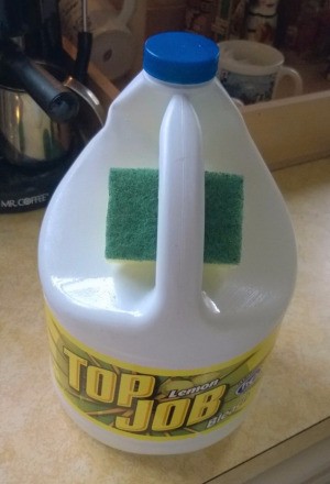A sponge stored in the handle of a bottle of cleaner.