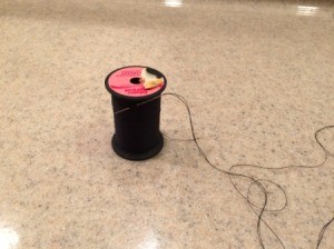 Pre-thread Your Needles - spool of black thread with a rethreaded needle stuck in the thread