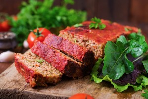 Vegetable meatloaf cut into slices surrounded by greens.