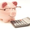 A pink piggy bank wearing glasses next to a calculator.