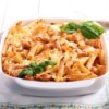 Baked Chicken Penne in a white dish with sprigs of fresh basil.