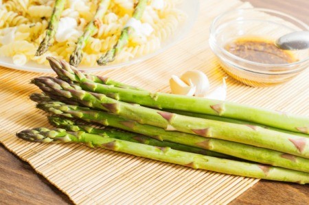 Asparagus in front of a penne dish and a sauce.