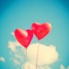 Two heart shaped red balloons in a blue sky with clouds.