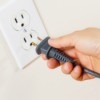 A hand ready to plug a cord into an electrical outlet.