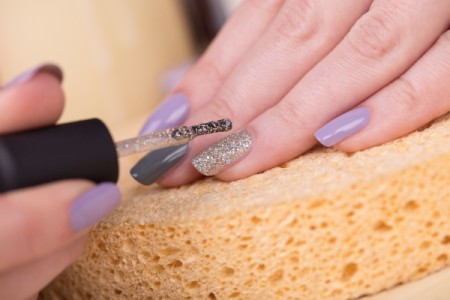 Woman applying silver glitter nail polish on ring finger.