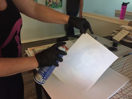 Spraying the back of the print with glue to adhere it onto the foam core.