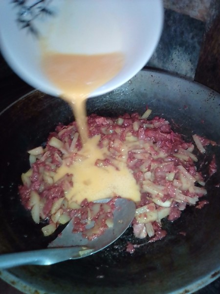 Whipped egg added to corned beef and potato in pan.