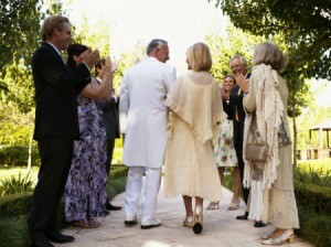 An older couple walking down the center aisle during an outdoor wedding ceremony.