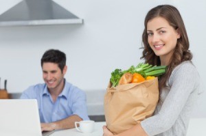 A couple with a computer and a bag of groceries.