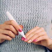 A woman in a grey sweater doing a manicure on herself.