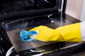 A person wearing rubber gloves, cleaning an oven.