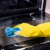 A person wearing rubber gloves, cleaning an oven.