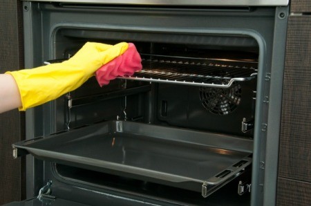 A rubber gloved hand cleaning oven racks with a pink sponge.