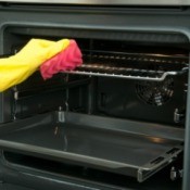 A rubber gloved hand cleaning oven racks with a pink sponge.