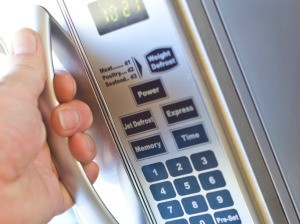 A hand pulling the handle on a microwave oven.