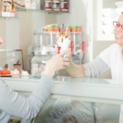 A woman working at an ice cream shop handing a cone to a customer.