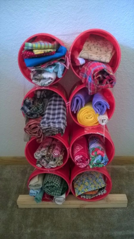 Using Coffee Tubs for Fabric Storage - stack of cans filled with fabric with a short piece of wood under the bottom row to give back tilt