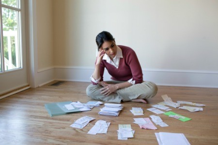 A woman looking at many receipts and paperwork on a wooden floor.