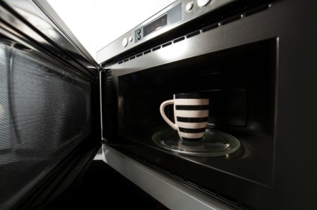 An open microwave oven, with a mug inside.