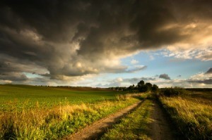 Storm clouds over green farmland with blue sky in the distance.