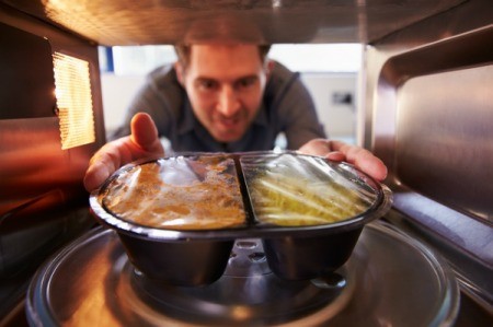 A man putting a frozen dinner in the microwave.
