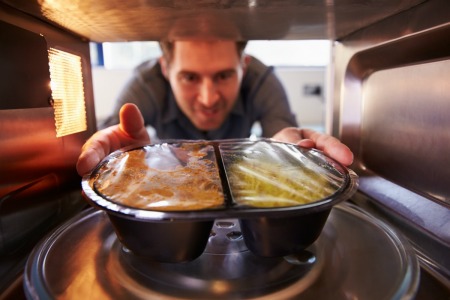 A man putting a frozen dinner in the microwave.