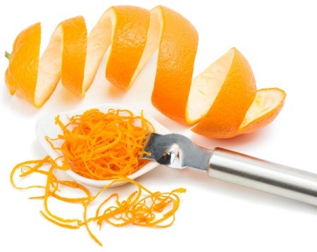 An orange zester with zest and a curly orange peel on a white background.