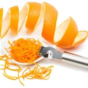 An orange zester with zest and a curly orange peel on a white background.
