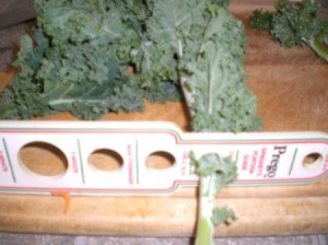A pasta measuring stick with holes, with a kale leaf inserted into one of the holes.