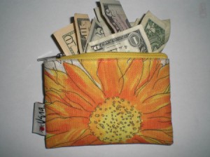 A orange and yellow flowered wallet with money sticking out the top.