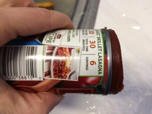 A can of tomato paste being squeezed out onto plastic wrap.