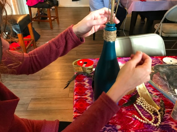 Twine being wrapped at the top of a painted wine bottle.