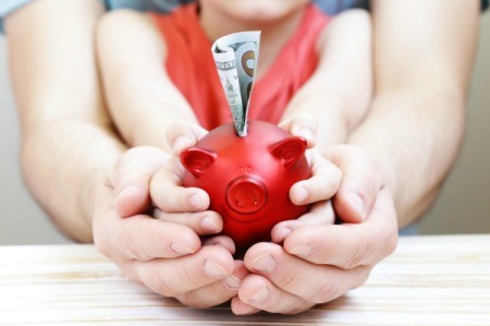 A red piggy bank being held by a child's hands and then an adult's hands.