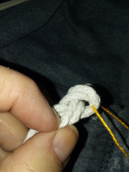 A piece of embroidery thread being inserted into a knot.