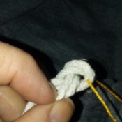A piece of embroidery thread being inserted into a knot.