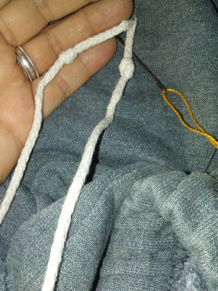 A untied length of string with a needle and embroidery thread next to it.