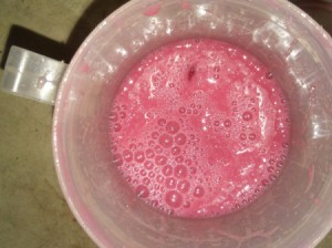 A pink colored milkshake in a cup.