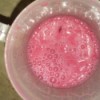 A pink colored milkshake in a cup.