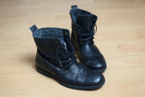 A pair of boots with black rubber soles on a wood floor.