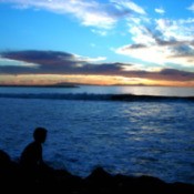 A boy silhouetted in front of the ocean at sunset.