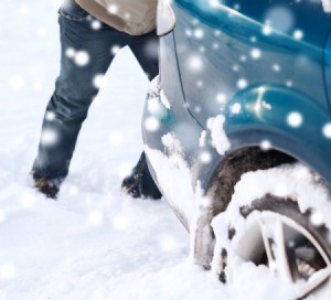 A man pushing a car that is stuck in the snow.