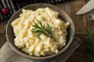 A bowl of mashed potatoes garnished with a sprig of rosemary.