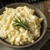 A bowl of mashed potatoes garnished with a sprig of rosemary.