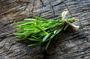 A sprig of rosemary on a wood surface.